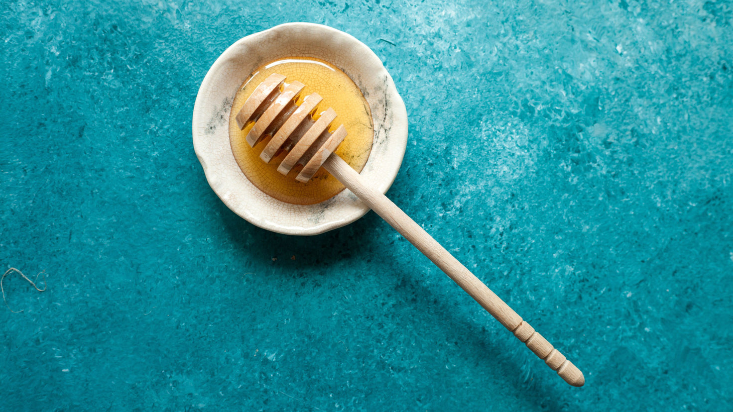 A wooden honey dipper in a small bowl of honey.
