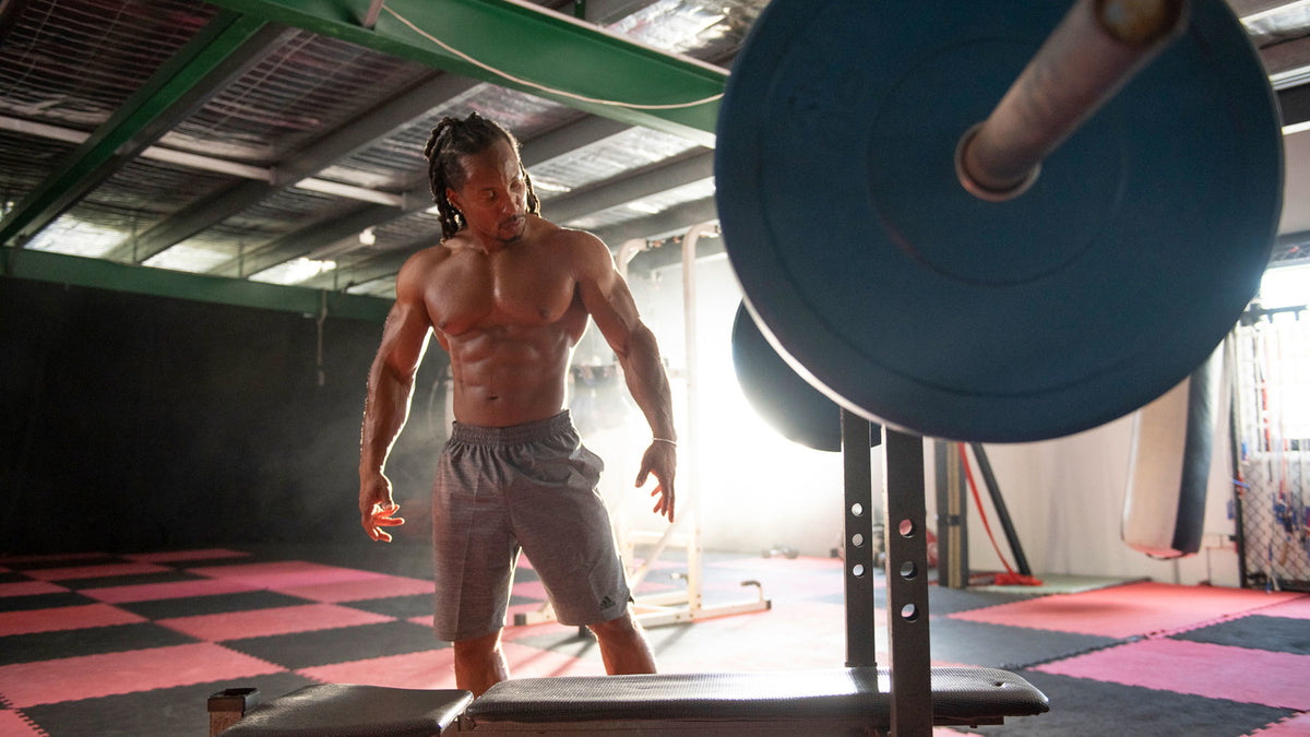 Muscular bodybuilder Torre Washington stands in a gym with his shirt off.