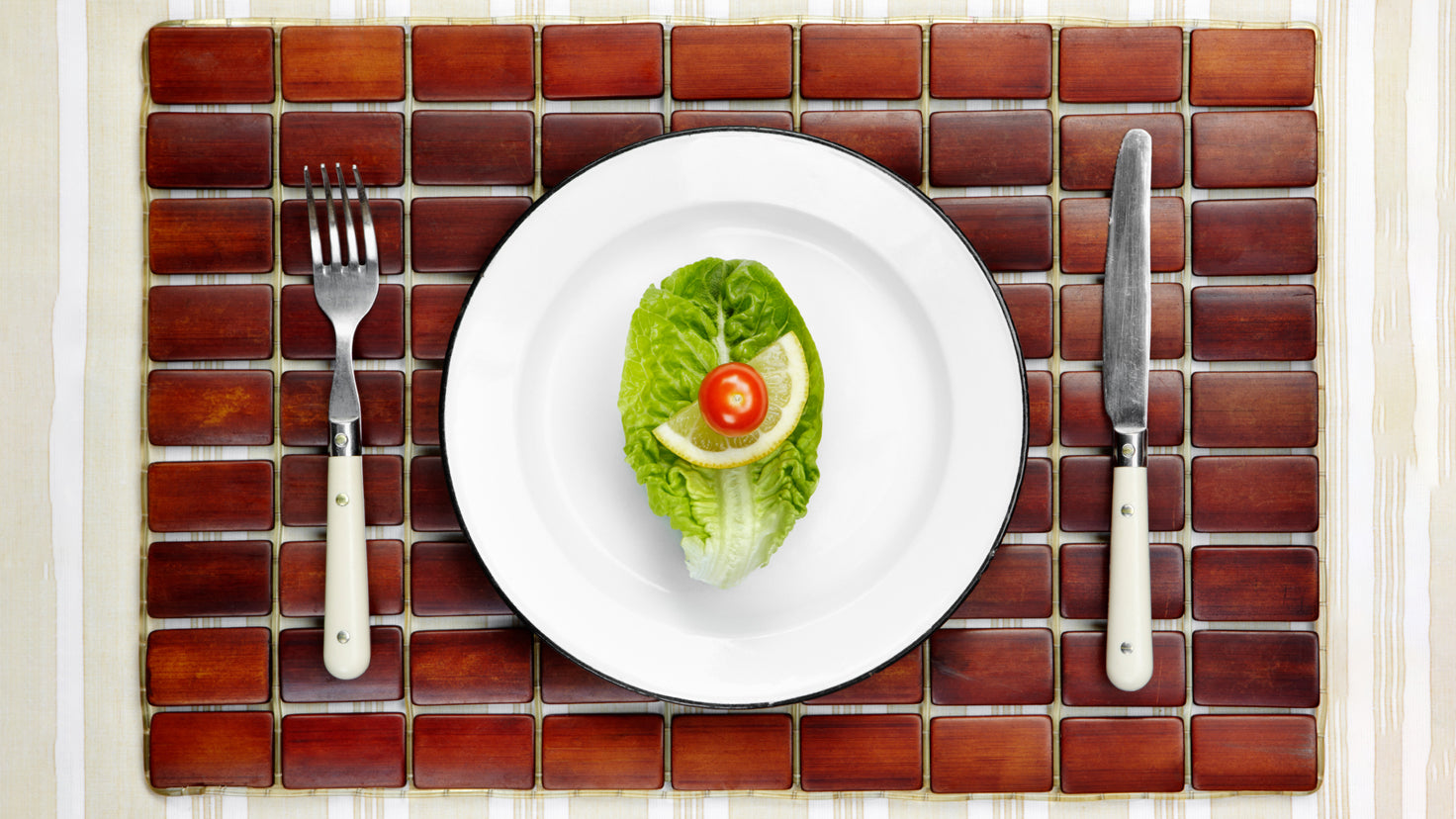 A lettuce leaf, lemon slice and single cherry tomato on a white plate.