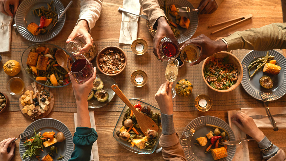 An overhead view of a large table of platters and plates of food, glasses of drinks, and the arms of
