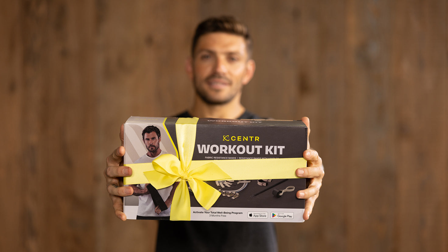 Centr Trainer Luke Zocchi holds out a Centr Workout Kit wrapped in a yellow ribbon.